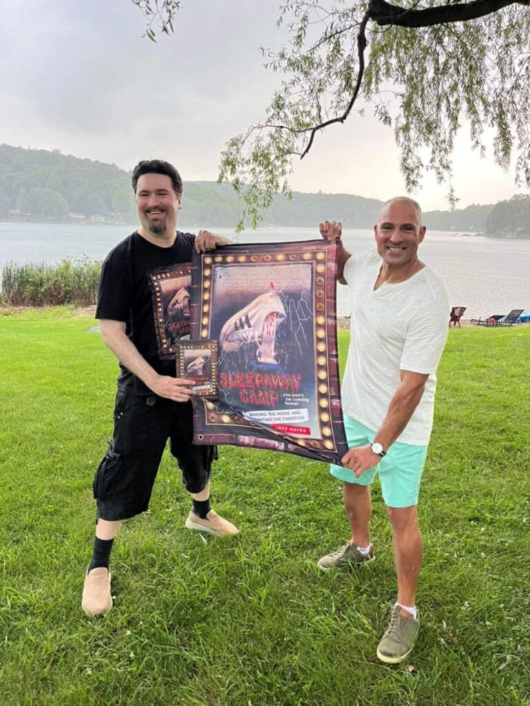 Jeff Hayes and Frank Saladino holding a Sleepaway Camp anniversary book poster at Camp Arawak